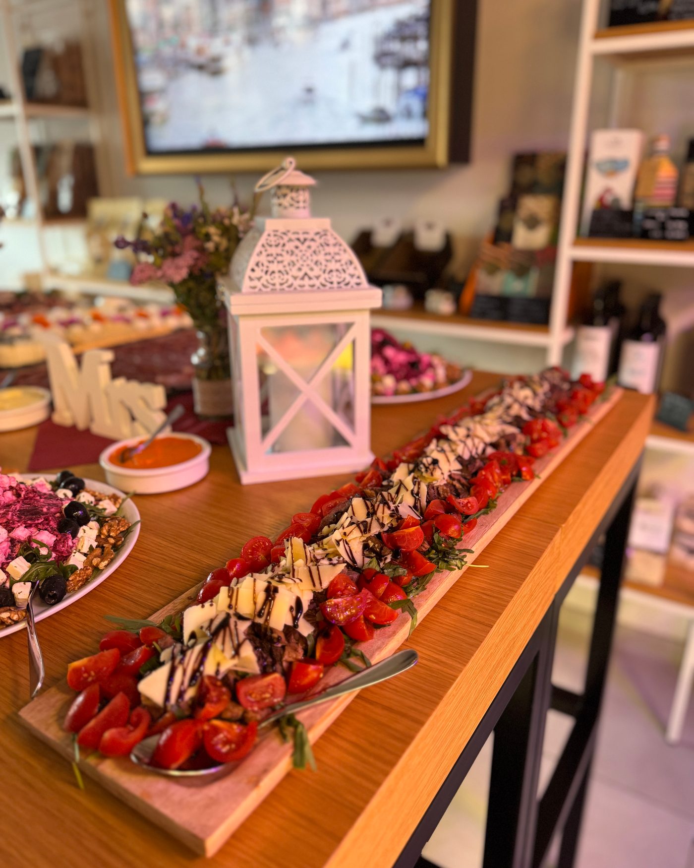 Festliches Buffet im Atelier: lange Holzplatte mit Tomaten, Mozzarella und Balsamico, Laterne und Blumen