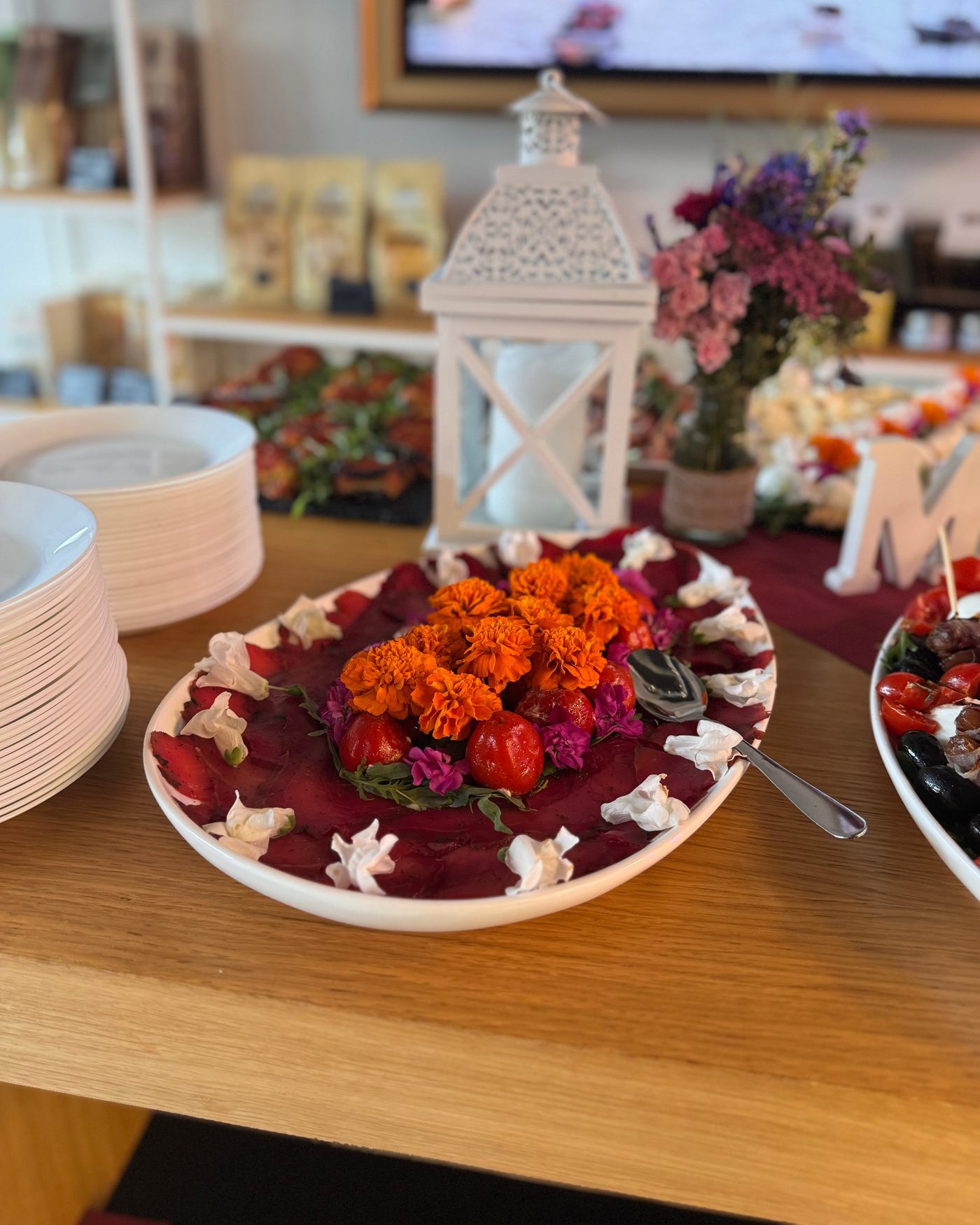 Buffetplatte mit Carpaccio, Tomaten und Tagetesblüten, daneben Tellerstapel