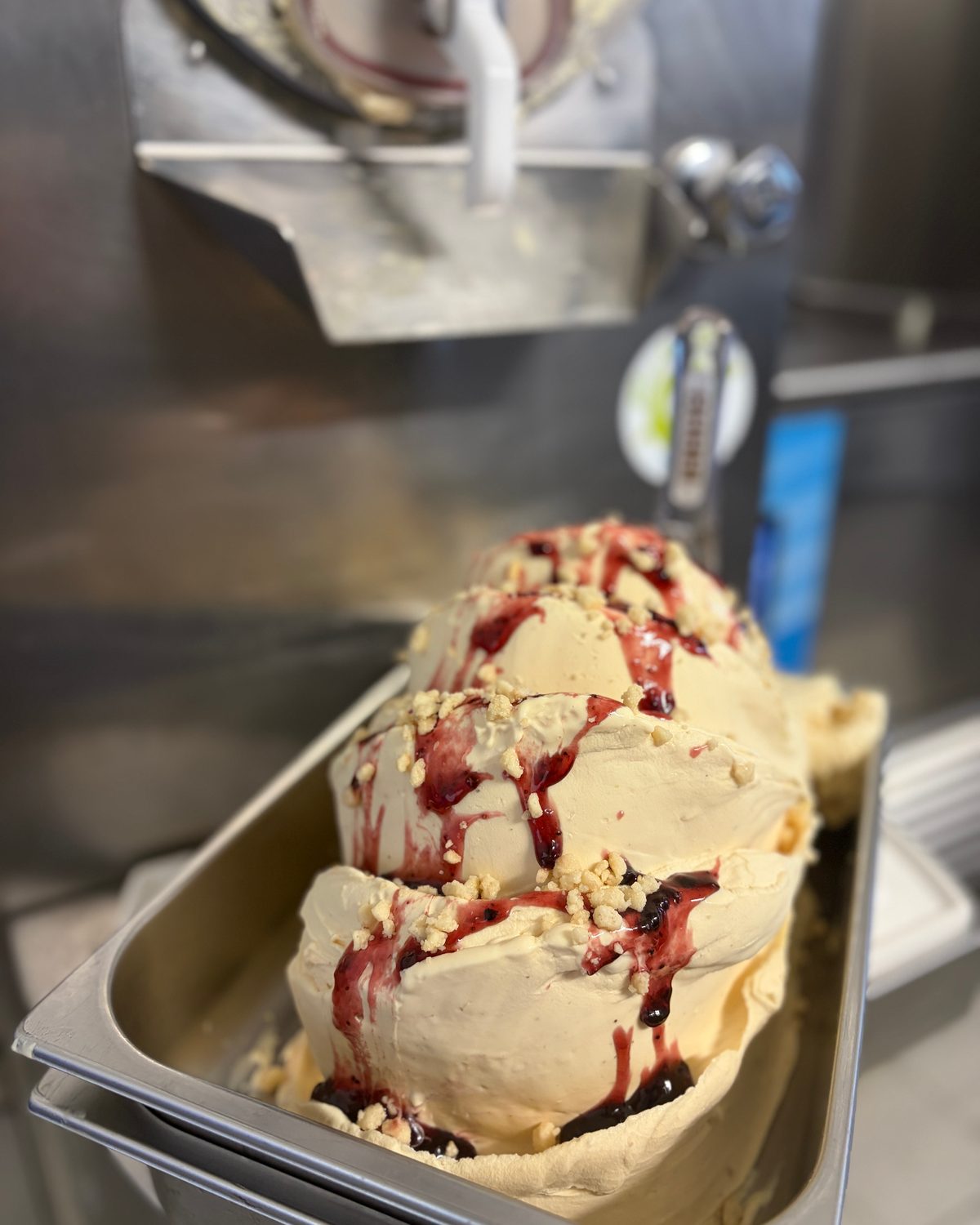 Frisch aus der Maschine gezogenes Gelato mit Beerensoße und Mandelsplittern