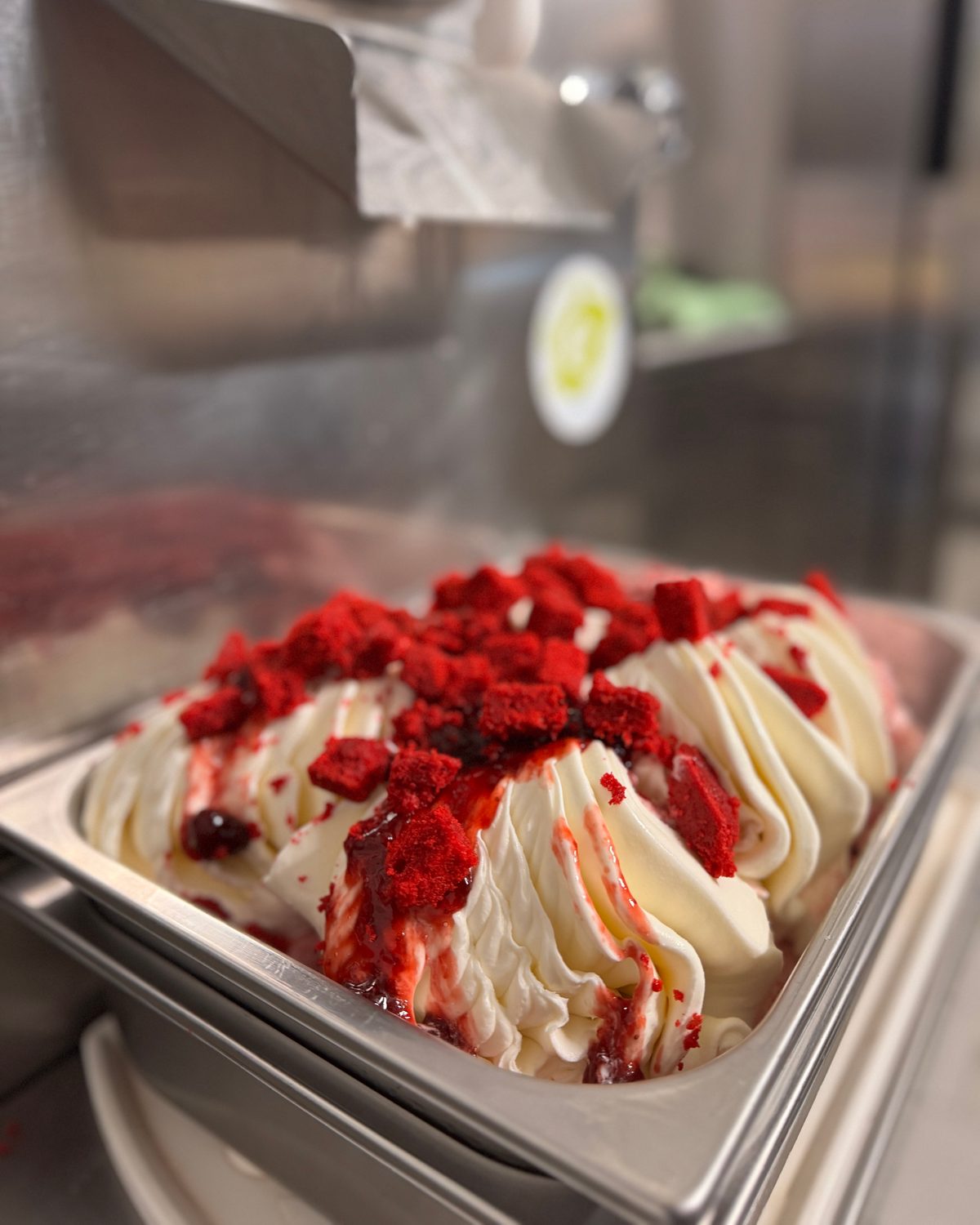 Helles Gelato in Wellen, belegt mit roten Kuchenwürfeln, direkt an der Eismaschine