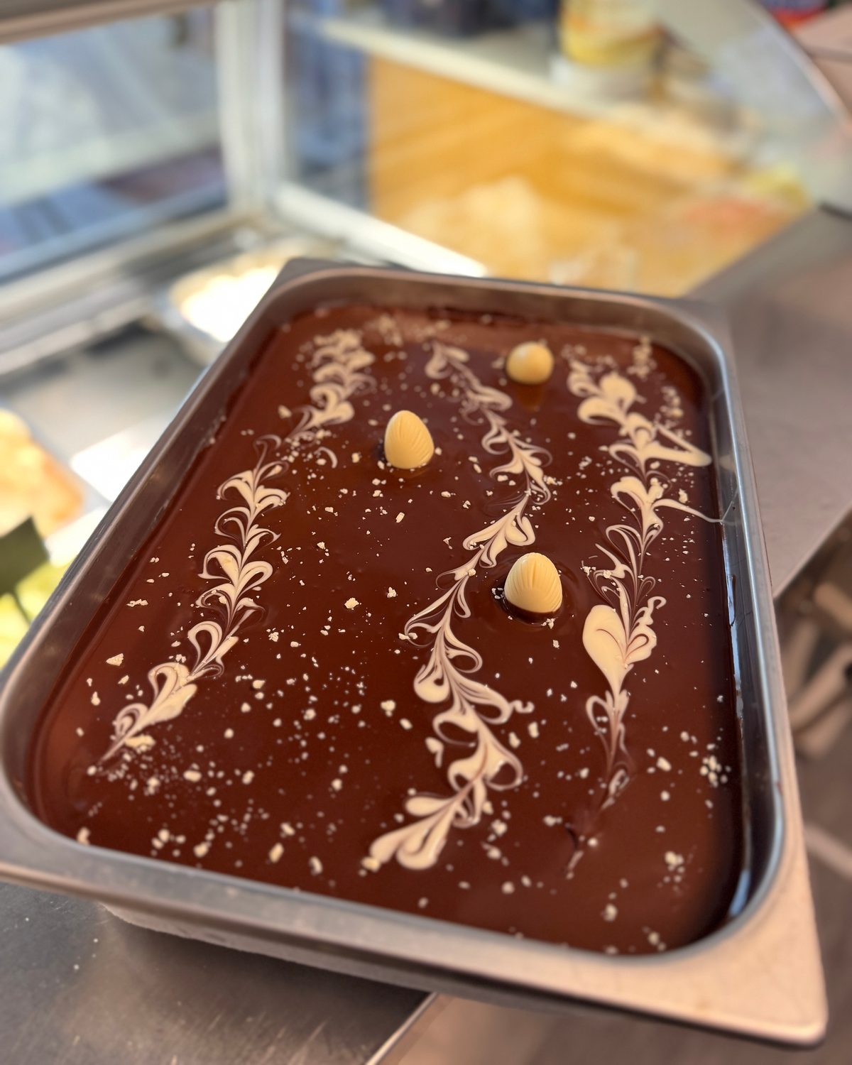 Schokoladen-Gelato in der Wanne, mit weißer Schokolade gemustert und Haselnüssen belegt