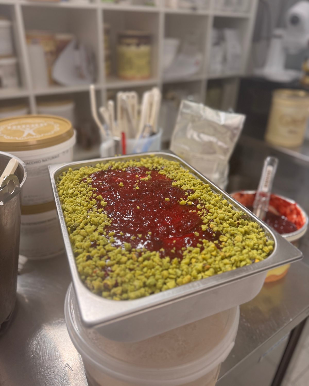 Wanne mit Pistazien-Gelato und Himbeerspiegel auf der Arbeitsfläche der Eisküche