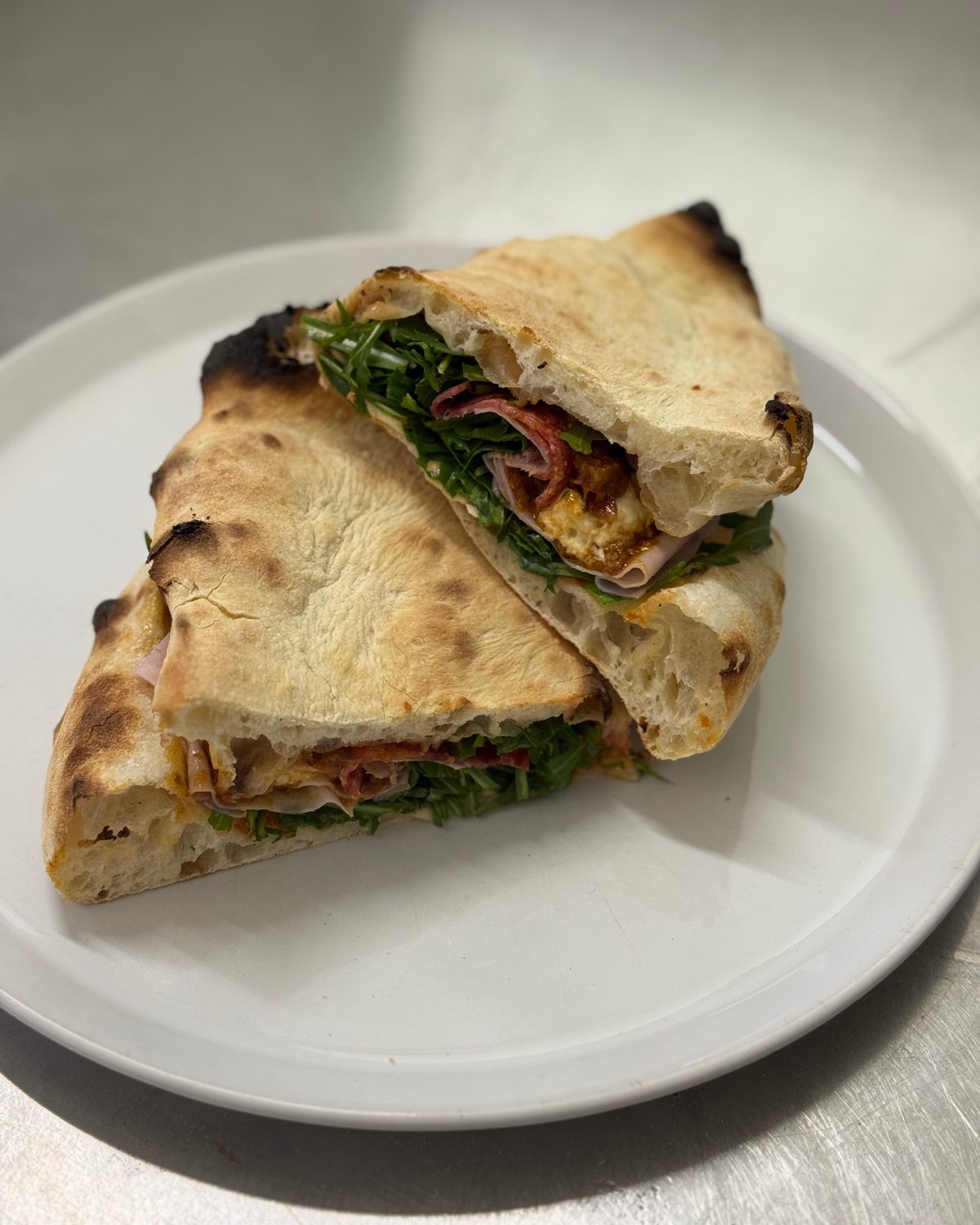 Gefülltes Pizzabrot mit Rucola und Schinken, aufgeschnitten auf weißem Teller