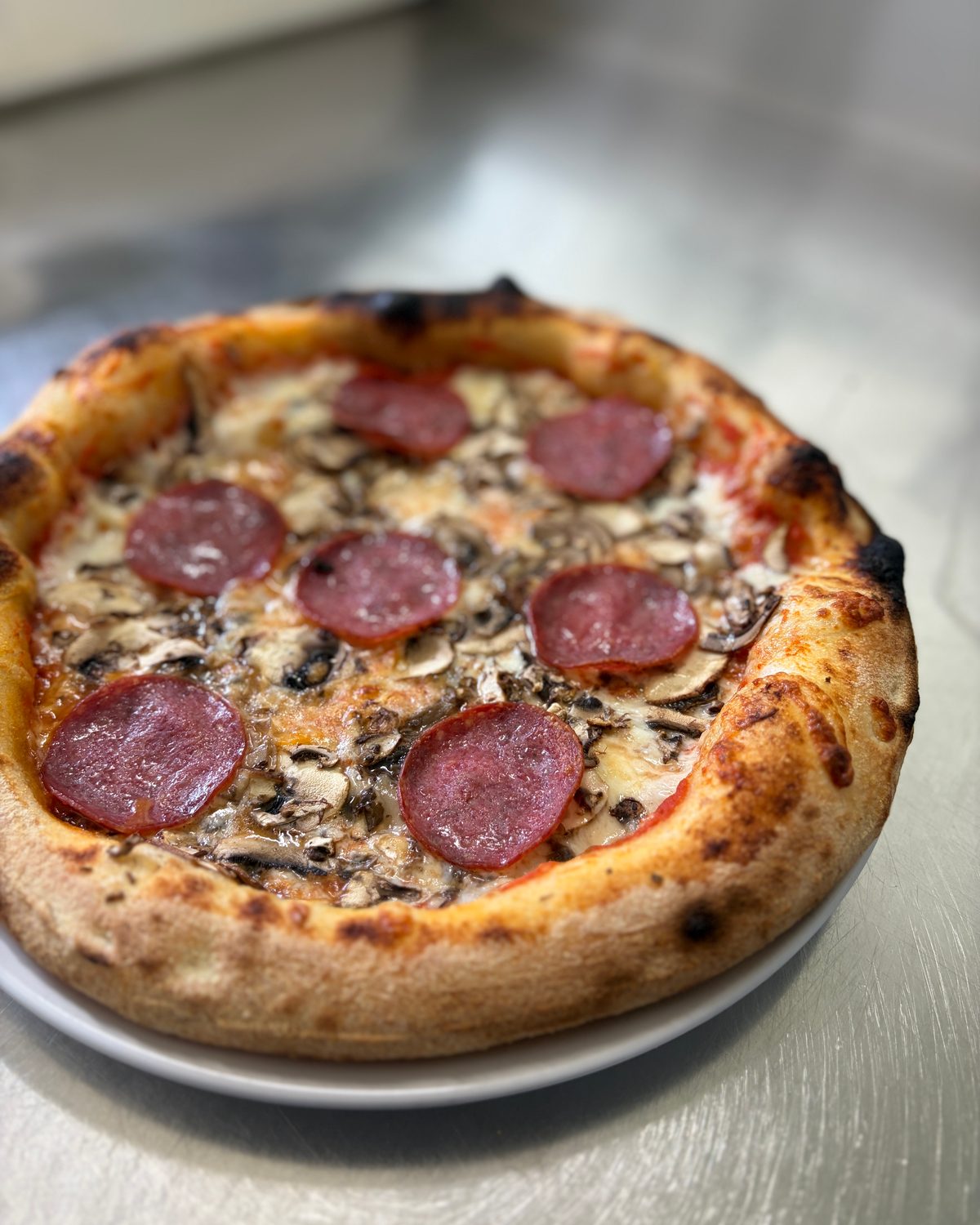 Pizza mit Salami und Champignons, hoher Rand mit dunklen Ofenblasen