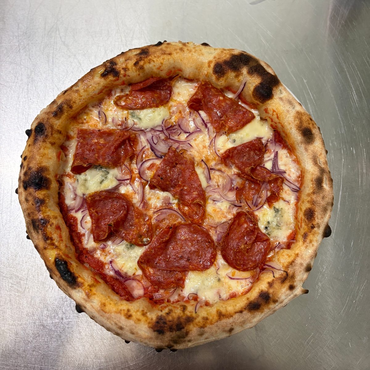 Pizza mit Salami, Gorgonzola und roten Zwiebeln von oben, dunkler Rand aus dem Ofen