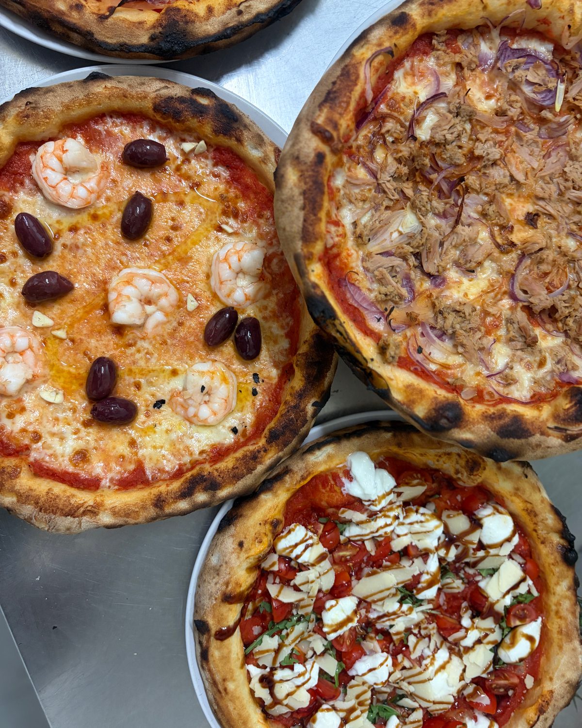 Drei frisch gebackene Pizzen auf der Edelstahlarbeitsfläche