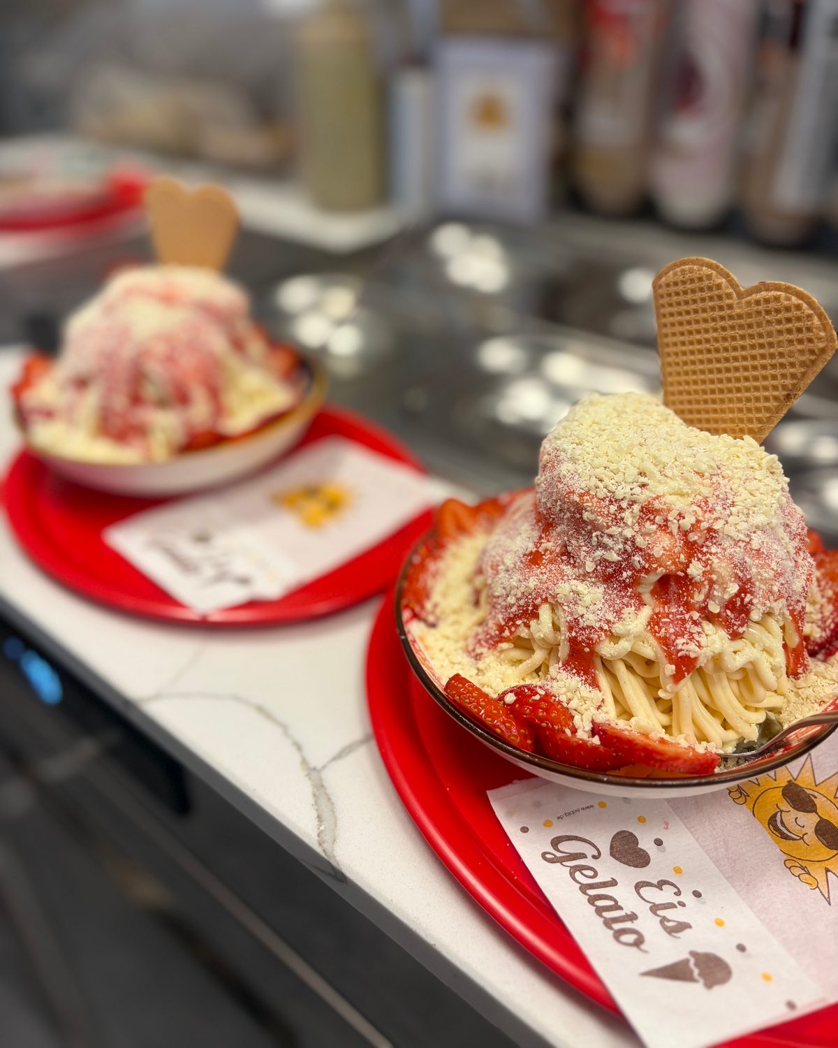 Zwei Spaghettieis mit Erdbeersoße, weißer Schokolade und Waffelherz auf roten Tellern