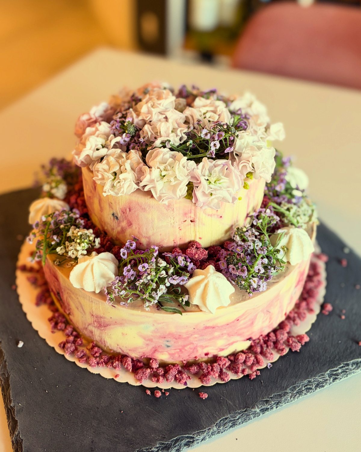 Zweistöckige Torte mit essbaren Blüten auf einer Schieferplatte