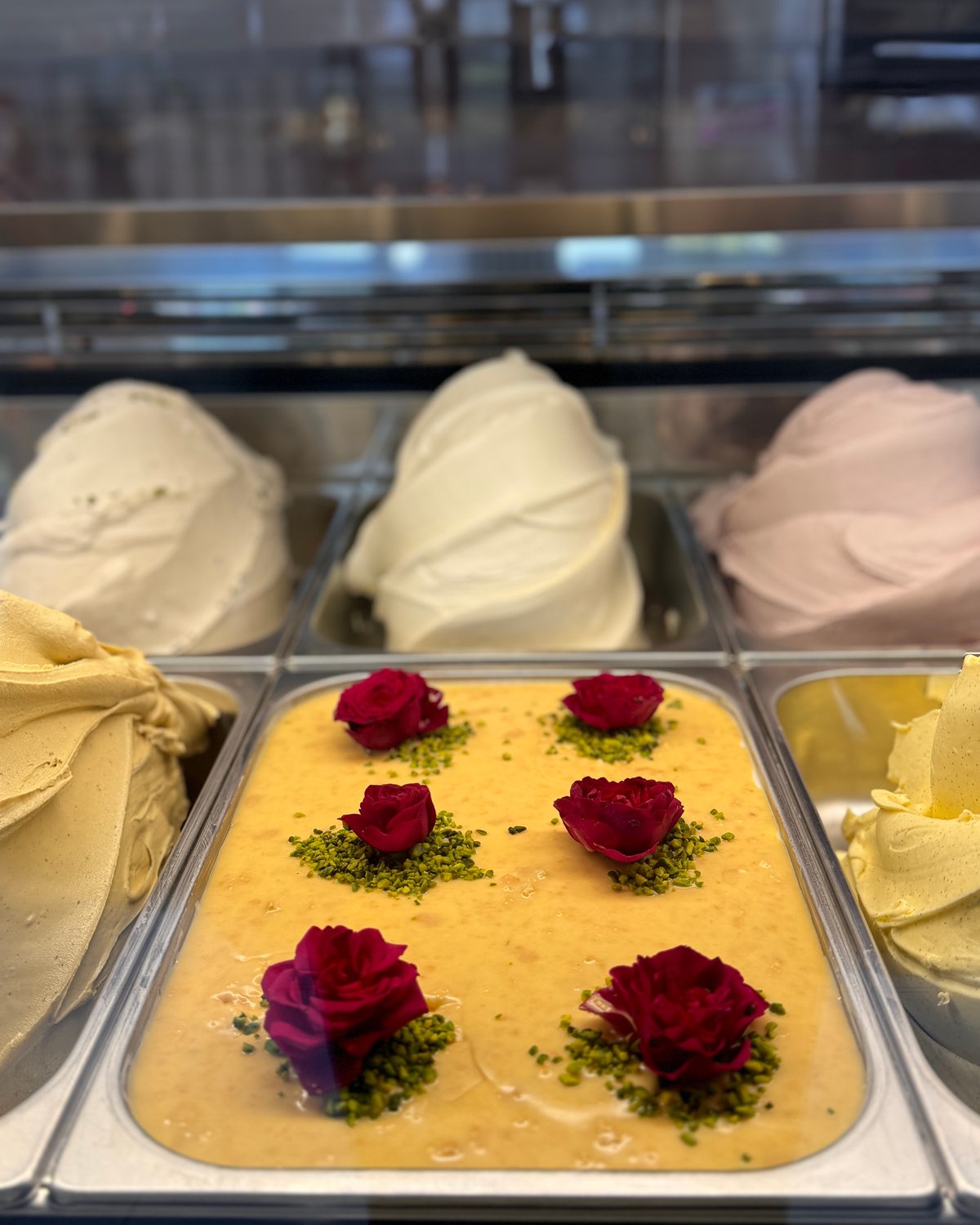 Gelato-Vitrine: Wanne mit hausgemachtem Eis, belegt mit roten Rosenblüten und gehackten Pistazien