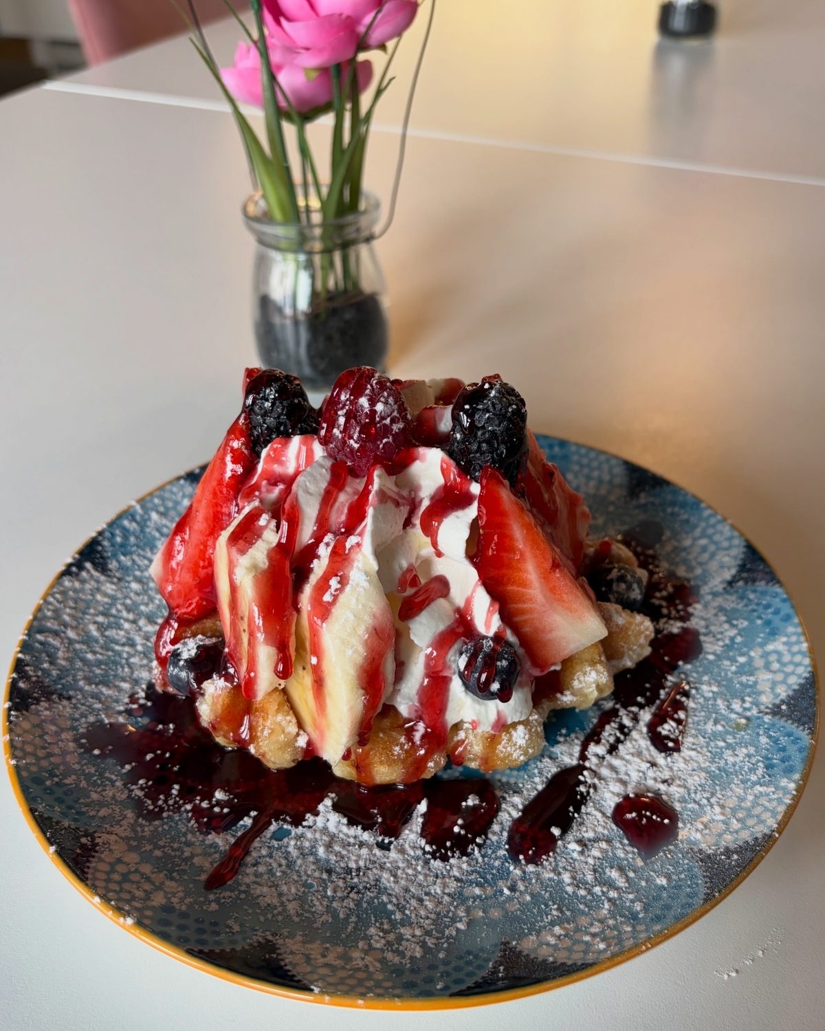 Waffel mit Gelato, Sahne und Beerensoße auf blau gemustertem Teller