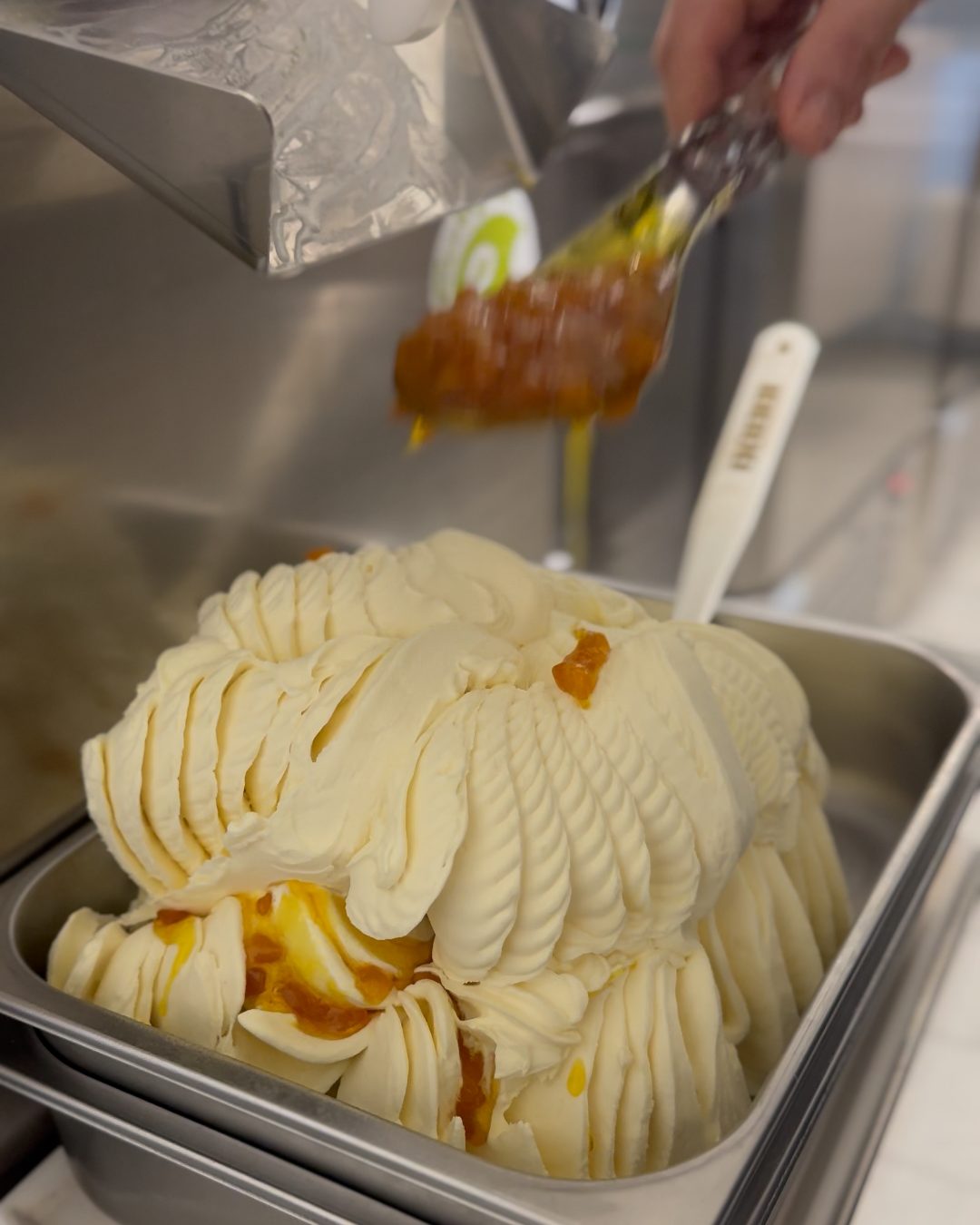 Soße mit Fruchtstücken wird über frisch gezogenes Gelato gegeben