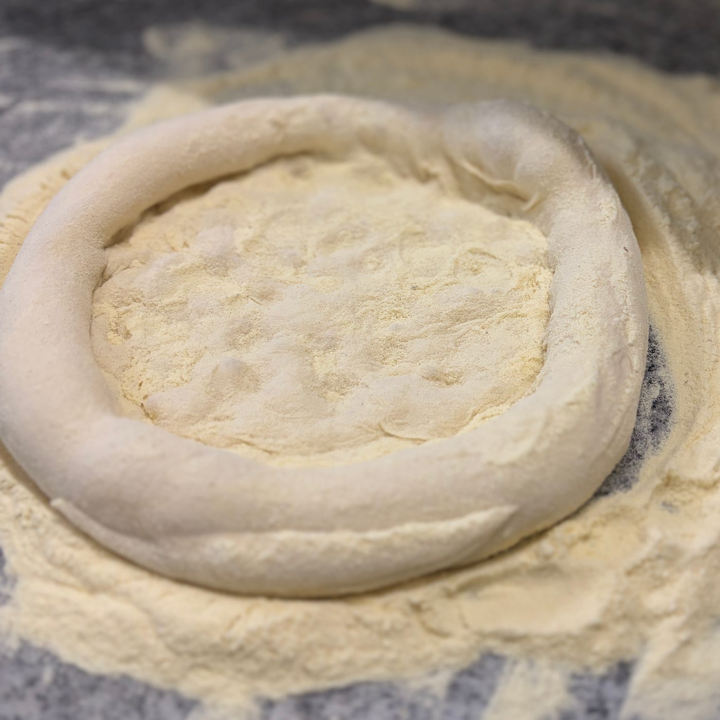 Ausgezogener Pizzateig auf bemehlter Arbeitsplatte, der Rand bereits geformt