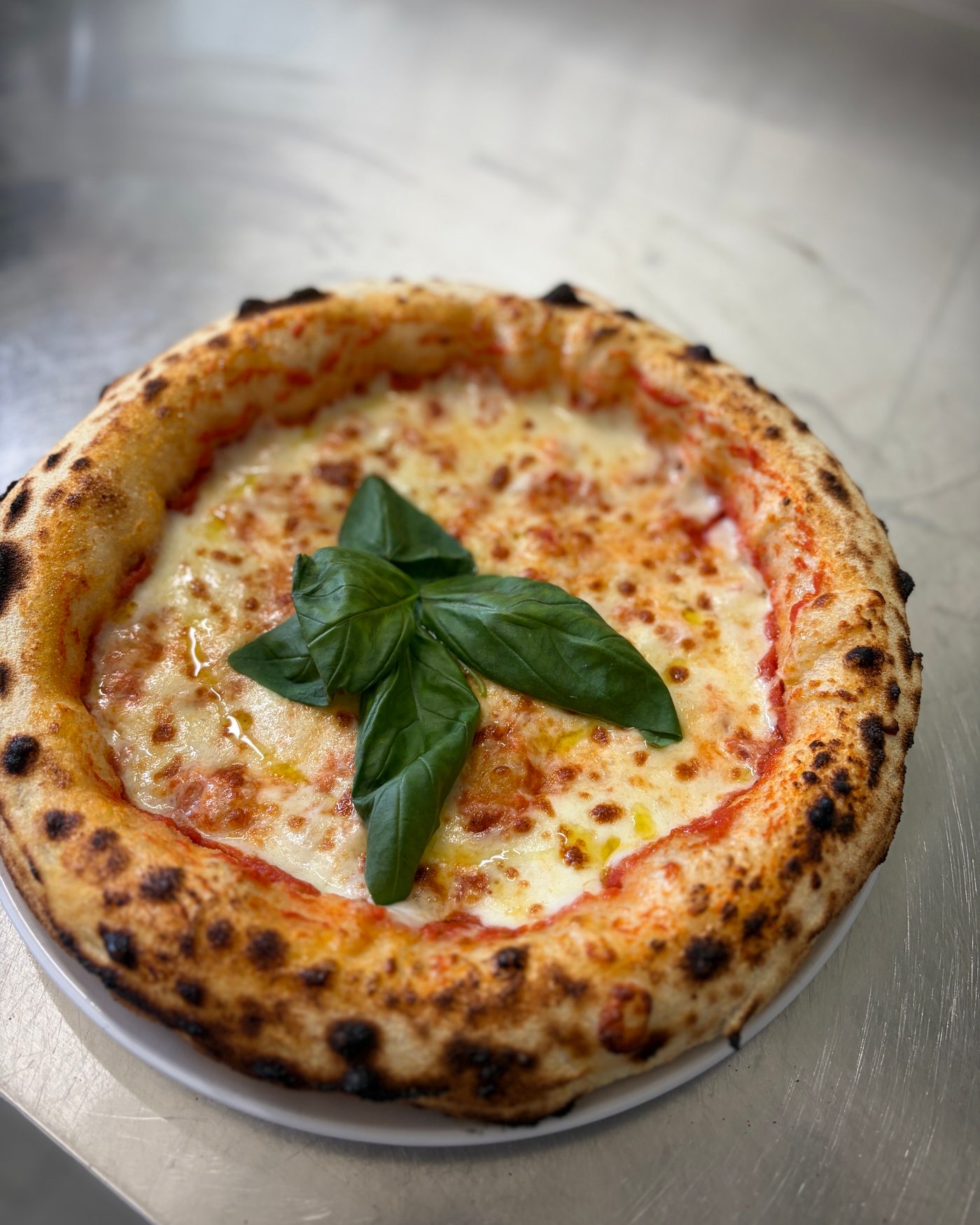 Pizza Margherita mit Basilikumblättern und hohem, gebräuntem Rand auf dem Teller
